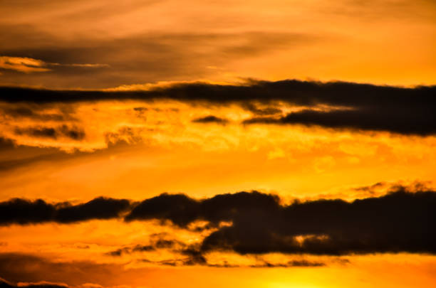 The sky is orange and the clouds are white. The sun is setting and the sky is filled with clouds