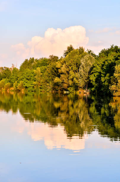 A beautiful lake with a cloudy sky in the background. The trees are lush and green, and the water is calm