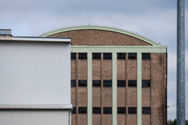 An industrial warehouse featuring an arched roof and a brick facade with vertical green accents.