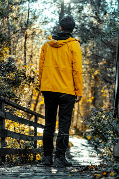 istock Man in yellow coat walking in forest among autumn trees. 2174018321