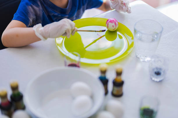 Child painting Easter eggs with colorful dye on green plate during festive activity at home.