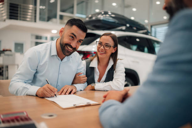 istock Delighted couple finalizes car transaction at dealership office. 2174040353