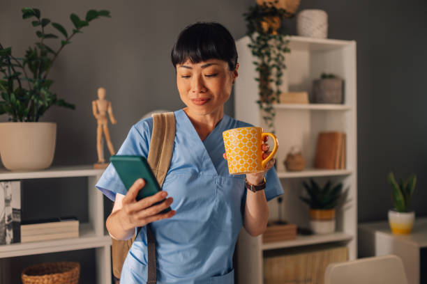 Asian nurse checking phone while holding a yellow cup in her modern space