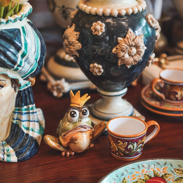 Frog prince. A cute frog prince ceramic wearing a crown displayed along with ceramic vases, dishes and glass on wooden table. Collective figurine for home decor. Vintage filter with slight film grain.