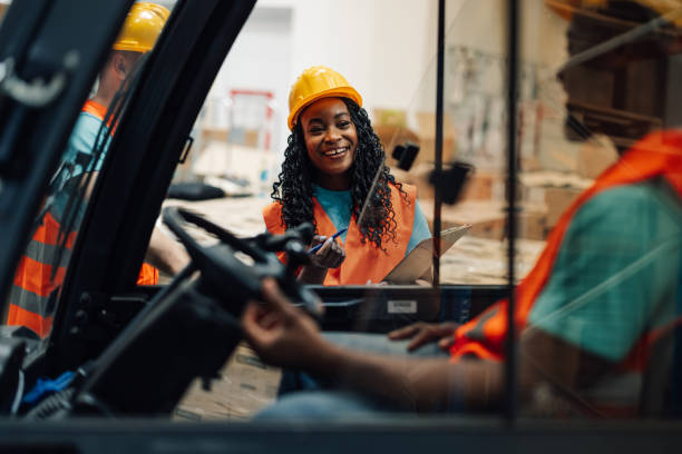 istock African american female worker smiles at forklift driver in warehouse. 2174042749