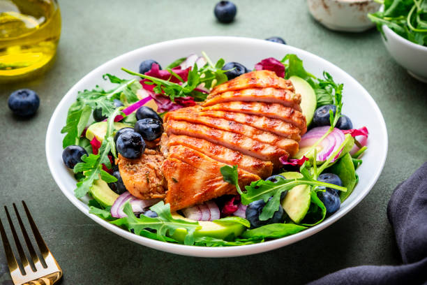 istock Green salad with grilled chicken, avocado and blueberries, rustic background, top view 2174046461