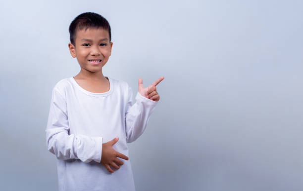 istock Smile boy wearing white shirt smiling indicate finger empty space and presenting, Studio shot on white background, Child pointing index out with copy space, Theme for advertising and promotion. 2174054897