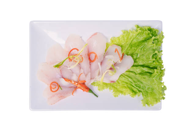 A rectangular plate holds thinly sliced white fish fillets arranged on a bed of lettuce, garnished with chili peppers and green onions.