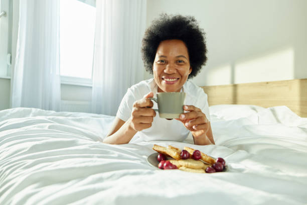 istock Happy black woman drinking morning coffee on a bed. 2174077396