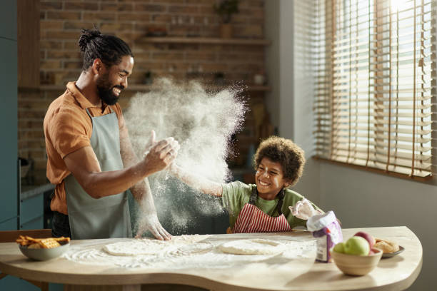 Happy black father and son having fun while making a cake in the kitchen.
