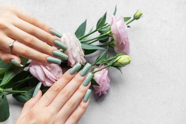 istock Elegant green manicured nails adorned with pastel flowers resting on a soft gray surface 2174079831