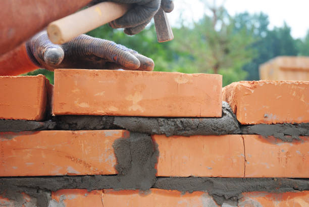 istock Bricklayer lays bricks on cement mortar. Builder hold brick with hand and knocks with a hammer from above during house wall construction. Bricklaying background with copy space. 2174081534