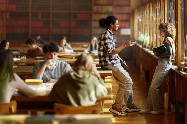 istock Happy college couple talking in a full library. 2174083693