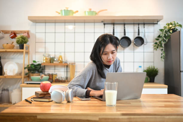 istock Happy young woman working on her laptop while sitting at a kitchen counter 2174097405