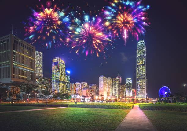 istock Nighttime view of a park with fireworks exploding over a city skyline, with illuminated skyscrapers and a Ferris wheel in the distance. 2174098606