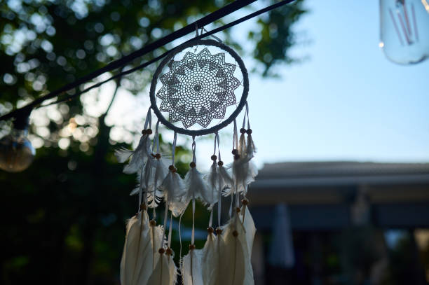 A beautiful dreamcatcher with delicate feathers sways gently in the breeze, hanging above a peaceful outdoor space illuminated by warm light.
