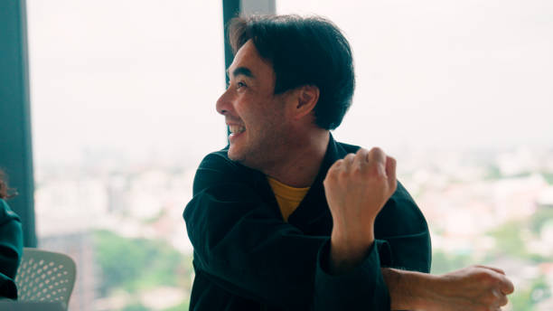 A young Asian man leading his team members to a round of exercise in the meeting room before an afternoon meeting.