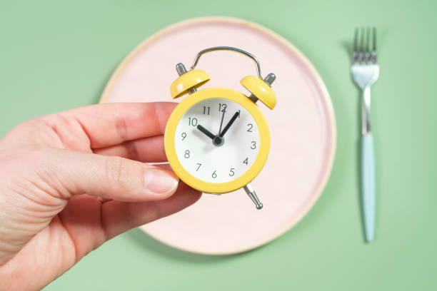 istock Female hand holding alarm clock against empty plate, intermittent fasting concept. 2174107475