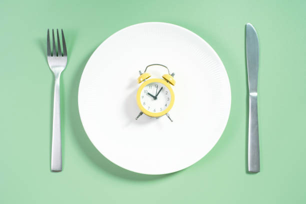 istock Empty plate with alarm clock on green background, intermittent fasting concept. 2174107482