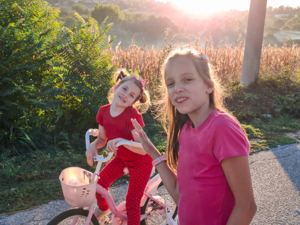 Two happy girls having fun while running and riding a bicycle through village road during late summer day