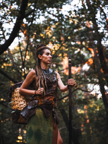 A warrior woman posing powerfully with her staff in a dense forest, her costume adorned with feathers and tribal elements.