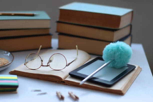 Various books, e-reader, reading glasses, stationery, cookies and cup of tea or coffee on the table. Back to school concept. Selective focus.