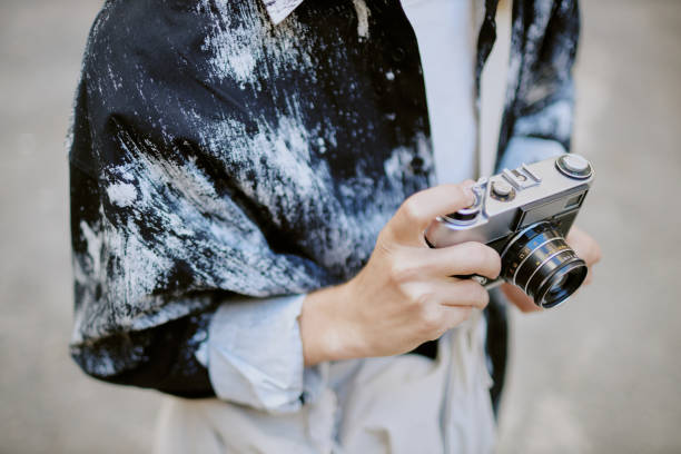 Close-up of a persons hand holding vintage camera while wearing a comfortable blue shirt. The focus is on the camera and the details of the persons shirt