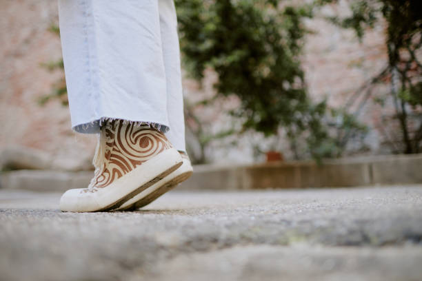Person wearing uniquely patterned shoes while walking on outdoor path with background of foliage and concrete. Image focuses on footwear design amidst natural surroundings