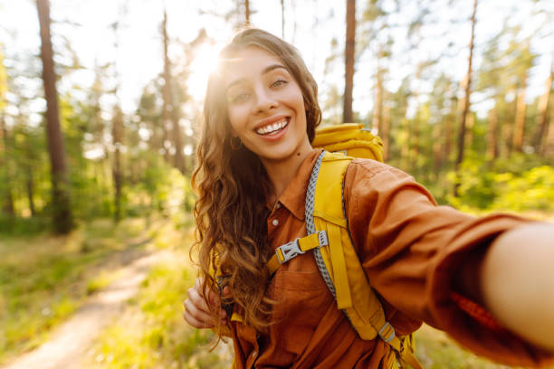 istock Selfie time! Young woman enjoying a sunny hike in a lush forest with a backpack. 2174120933