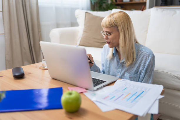 istock Young businesswoman holding smartphone while working with laptop at home office desk, using cross platform responsive design apps for project analysis, analyzing cloud data statistics. Freedom concept 2174120950