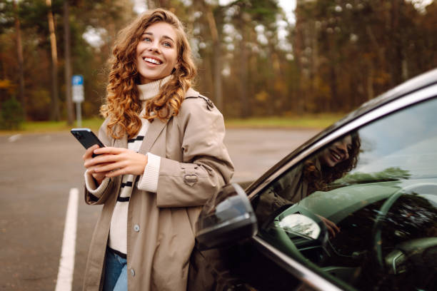 istock Young woman enjoying a cheerful moment while using her smartphone beside a parked car in a scenic forest setting. 2174122159