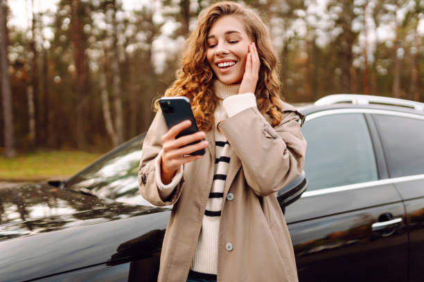 istock Young woman enjoying a cheerful moment while using her smartphone beside a parked car in a scenic forest setting. 2174122169