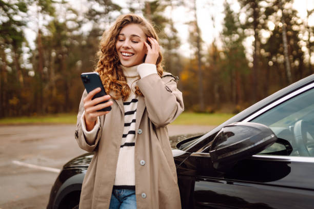 istock Young woman enjoying a cheerful moment while using her smartphone beside a parked car in a scenic forest setting. 2174122176