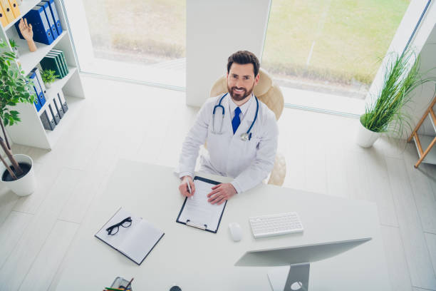 Photo of expert qualified doctor guy sit table write checklist report in hospital room Photo of expert qualified doctor guy sit table write checklist report in hospital room. qualified report stock pictures, royalty-free photos & images