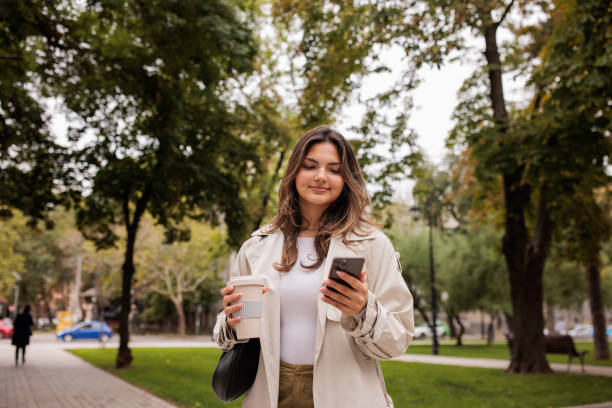 istock Young woman using her phone while walking in a park 2174130029