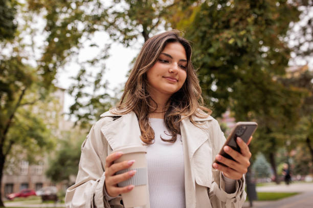 istock Young woman using her phone while walking in a park 2174130040