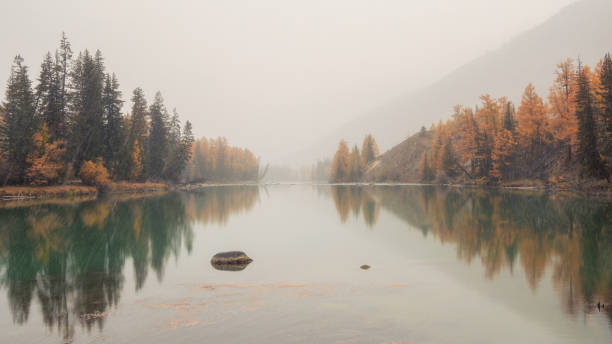 Soft focus. Snow is blowing. Quiet, calm autumn river. Beautiful panoramic misty mountain landscape with wide river. Dark atmospheric view to great river among mountains in rainy weather.