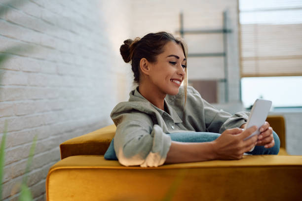 istock Smiling woman text messaging on mobile phone at home. 2174136833