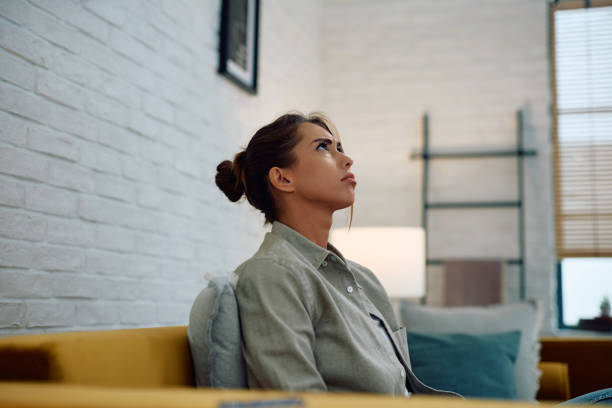 istock Upset woman sitting on the sofa at home and looking up. 2174136854