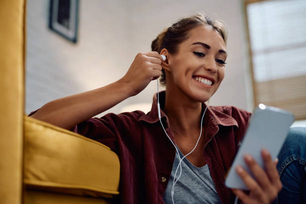 Happy woman using earphones while listening music over mobile app.