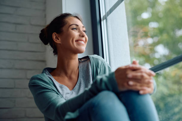 istock Smiling woman day dreaming while relaxing by the window at home. 2174137175