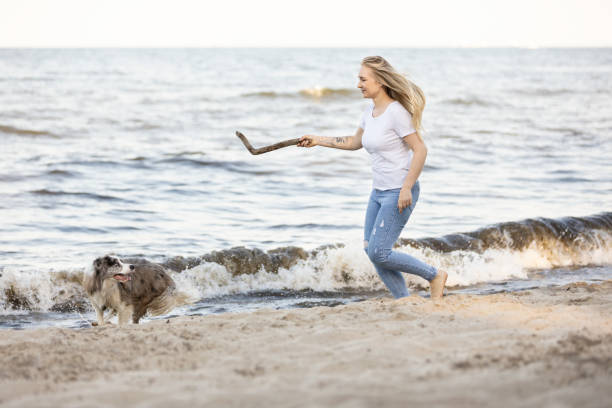 Young woman having fun on sandy beach with her dog catching a stick.