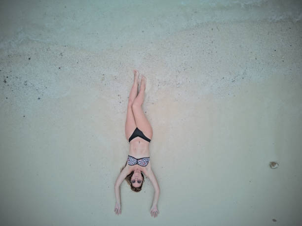 High angle view of a woman with sun hat sunbathing while relaxing in sand during summer day on the beach. Copy space.