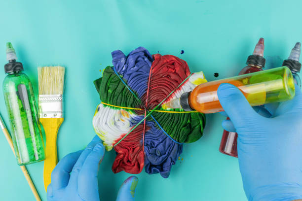 istock Vibrant Tie-Dye Creation Process with Gloves, Paint Bottles, and Brushes on Turquoise Background 2174147550