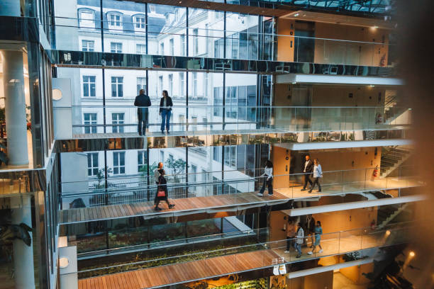 Diverse Professionals in Multi-Level Office Complex Professionals of varying genders engage in discussions and walk through a multi-tiered office environment, highlighting modern corporate attire and dynamic work settings. african american architecture stock pictures, royalty-free photos & images