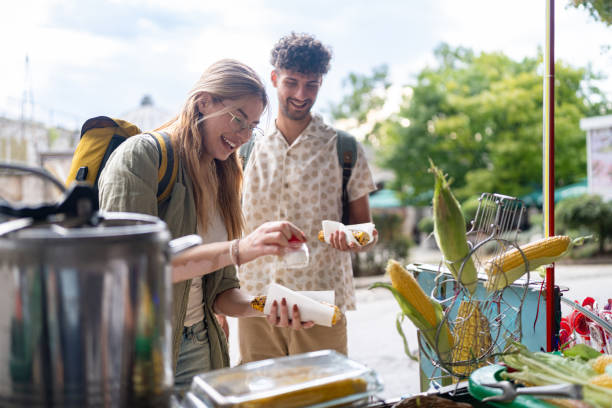 istock Young tourist couple with backpacks, buying corn from a street stall while exploring historical sights. 2174152934