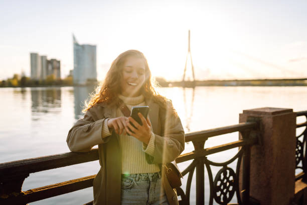 istock Young woman enjoys a sunny day by the river, using her smartphone. 2174156135
