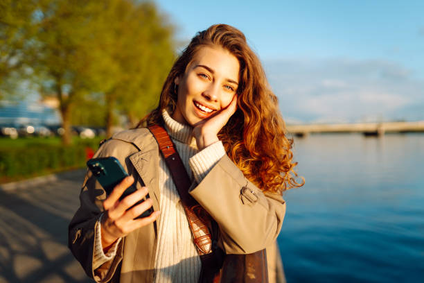 istock Young woman enjoys a sunny day by the river, using her smartphone. 2174156149
