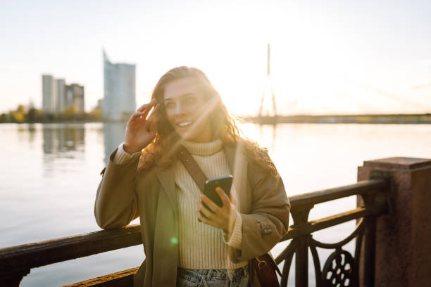 istock Young woman enjoys a sunny day by the river, using her smartphone. 2174156153