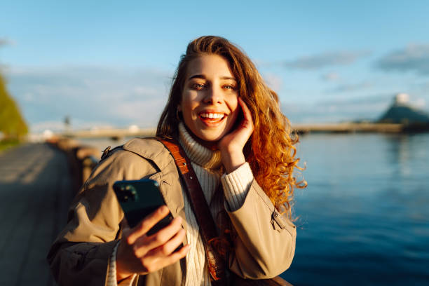 istock Young woman enjoys a sunny day by the river, using her smartphone. 2174156161